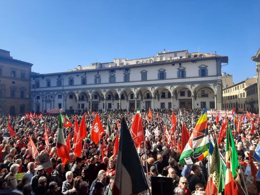 piazza santa croce a firenze piena di persone con bandiere rosse e multicolore