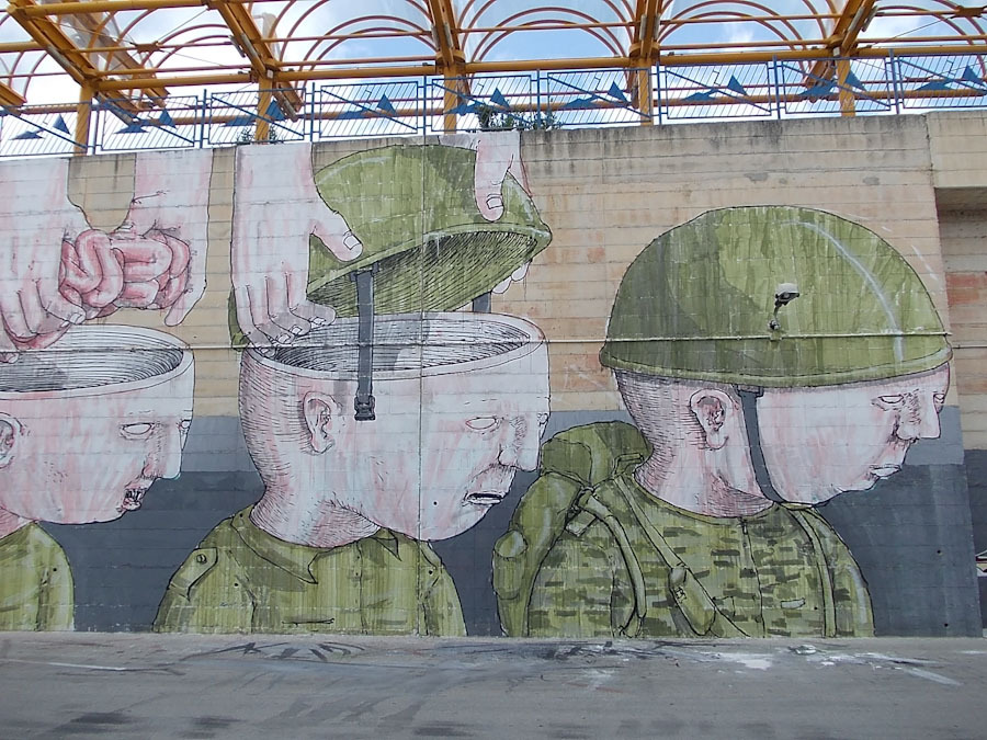 murales che rappresenta tre immagini di persona di profilo, a cui in sequenza delle mani tolgono il cervello dalla scatola cranica e mettono l'elmetto